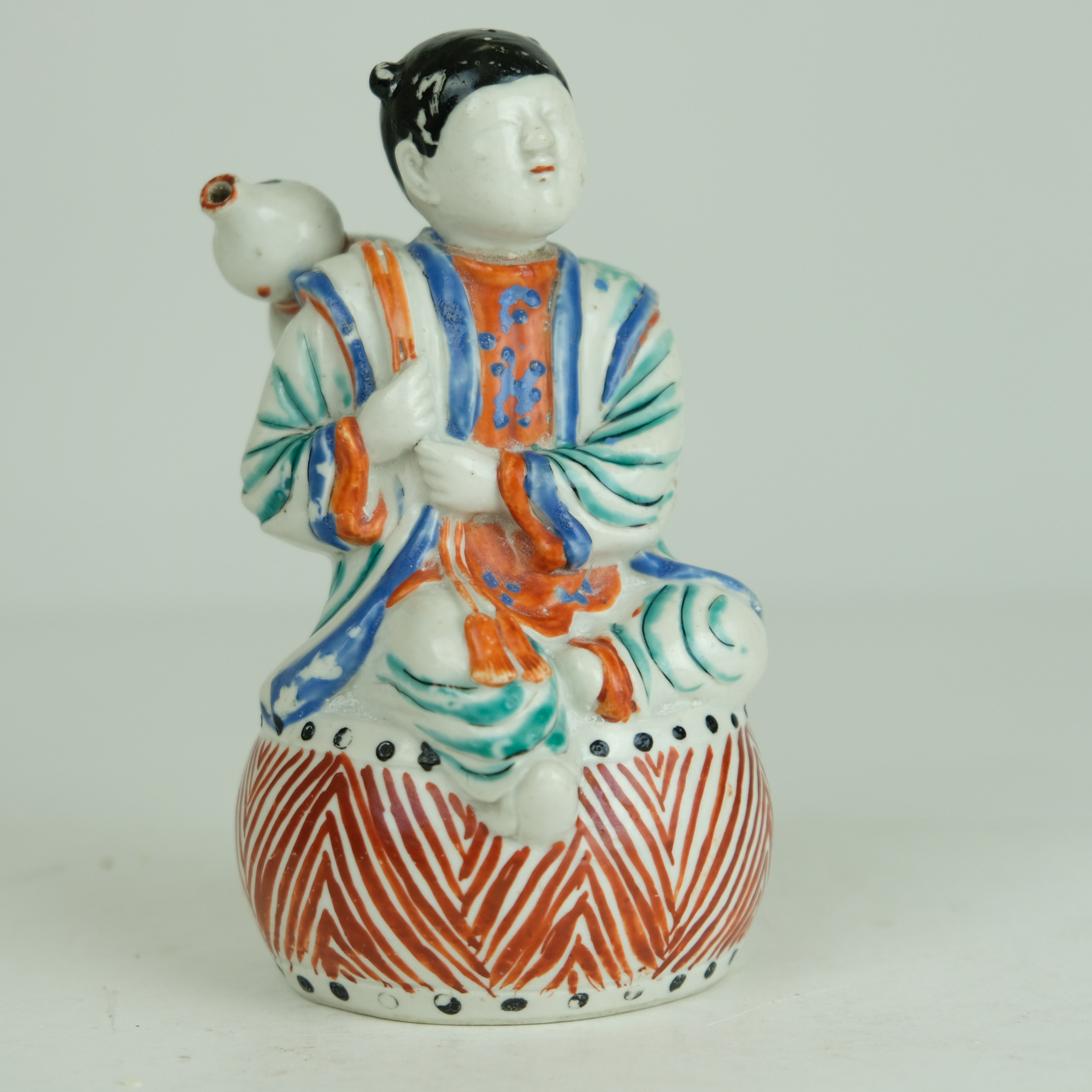 Japanese Kakiemon figure of a boy sitting on a drum.